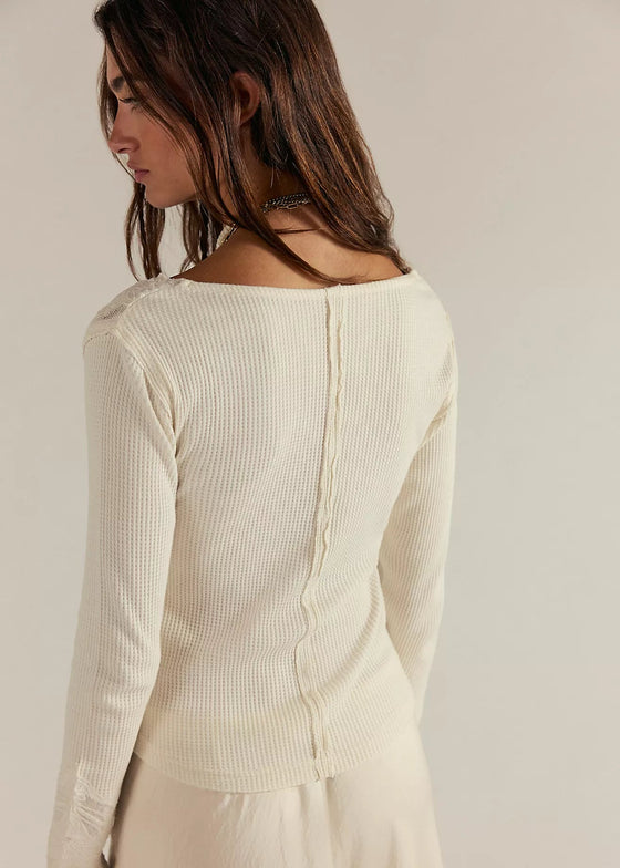 Woman wearing a cream ribbed long-sleeve top against a plain background