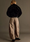 Person wearing a black fur coat and leopard print pants on a plain background