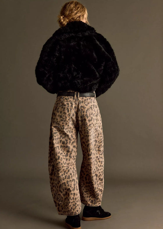 Person wearing a black fur coat and leopard print pants on a plain background