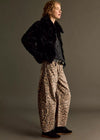 Person wearing a black fur coat, dark shirt, and leopard print pants on a gray background