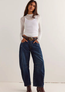  Woman wearing a white long-sleeve top, blue jeans, and brown boots against a white background