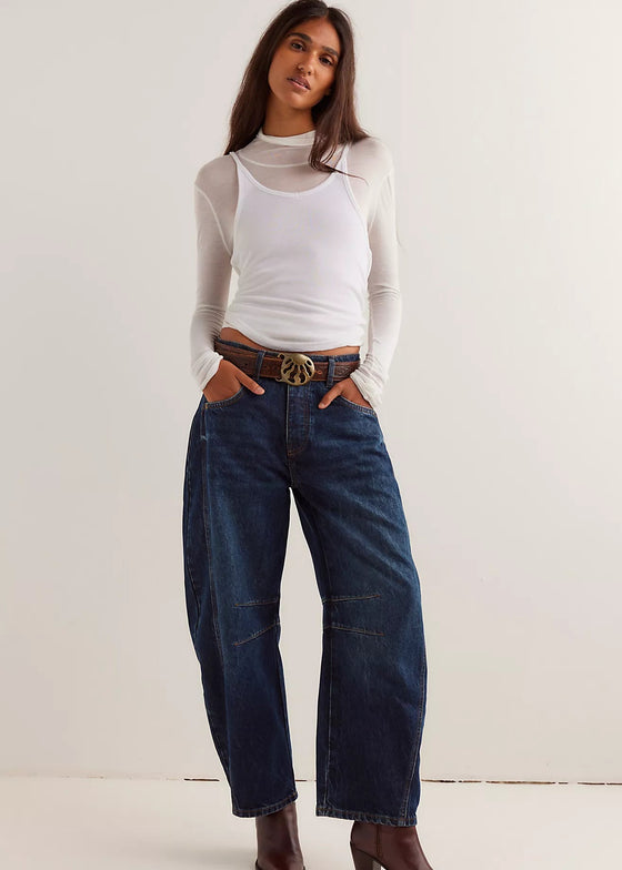 Woman wearing a white long-sleeve top, blue jeans, and brown boots against a white background