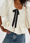 White blouse with black ribbon and ruffles worn by a person, with a plain background