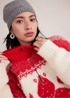 Woman wearing a red and white patterned sweater with a gray knit hat.