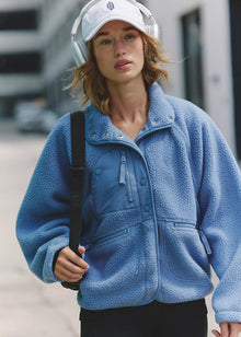  Person wearing a blue fleece jacket and white cap with headphones, standing outdoors.
