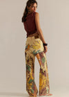 Woman wearing a sleeveless top and colorful floral pants on a beige background