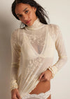 Woman wearing a sheer lace bodysuit against a plain background