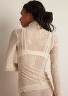 Woman wearing a sheer white lace top against a plain background