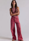 Woman wearing a pink striped tank top and pink high-waisted jeans against a plain background