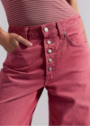 Close-up of pink jeans with button details on a plain background