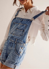 Person wearing a denim overalls with a white shirt underneath on a plain background