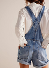 Person wearing denim overalls and a white shirt on a plain background