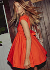 Woman wearing an orange dress standing against a wooden wall.