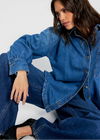 Woman wearing a blue denim outfit sitting on a white stool against a white background