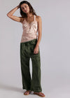 Woman wearing a pink top and green pants against a plain background