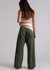 Person wearing green wide-leg pants and a pink top on a plain background