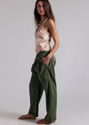 Woman wearing a pink top and green pants on a plain background