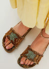 Brown sandals with green pattern worn by a person in yellow pants on a white background