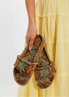 Pair of patterned slippers held by a person wearing a yellow dress.