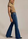 Woman wearing a beige top and blue flared jeans on a plain background