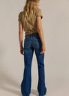 Person wearing a brown shirt and blue flared jeans on a beige background