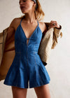Woman wearing a blue denim romper with a beige jacket over her shoulder.