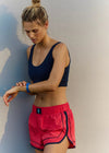 Woman wearing a navy sports bra and red shorts against a neutral background