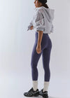 Person wearing a gray hoodie, purple leggings, and black sneakers on a white background