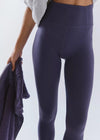 Person wearing dark purple leggings holding a matching towel on a white background