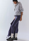 Person wearing a gray hoodie, purple leggings, and black sneakers on a white background