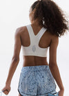 Person wearing a white sports bra and blue patterned shorts on a plain background