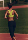 Woman running on a track wearing a yellow sports bra and black leggings.