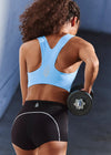 Person wearing a blue sports bra and black shorts holding a dumbbell against a gray background