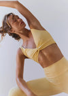Woman in a yellow sports bra and leggings posing against a white background