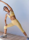 Woman in yellow athletic wear stretching against a white wall.