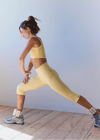 Woman in yellow athletic wear stretching on a wooden floor against a white wall