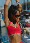 Woman in a red bikini top and shorts standing by a marina with boats in the background.