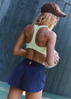 Woman in athletic wear holding a tennis racket against a textured wall.