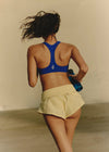 Person wearing a blue sports bra and yellow shorts holding a water bottle.