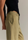 Person wearing olive green pants and a black top against a neutral background