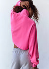 A person shown from the back wearing a bright pink cropped sweatshirt and light gray sweatpants against a plain white wall.