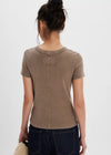 Person wearing a brown t-shirt with a small logo on the back, standing against a plain white background.
