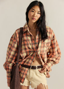  Woman wearing a plaid shirt and shorts with a brown bag against a plain background
