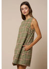 A woman modeling a sleeveless, knee-length plaid dress in sage green with orange and white windowpane lines, set against a solid beige studio background.