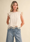Woman wearing a cream top with lace details and blue jeans on a beige background