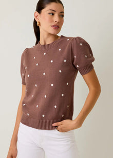  Woman wearing a brown sweater with white polka dots and white pants on a plain background