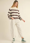 Woman wearing a striped sweater and white pants on a beige background