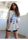 Woman wearing a white oversized t-shirt with graphics and text, standing indoors.