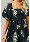 Black dress with white floral pattern worn by a person