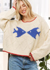 Woman wearing a cream sweater with blue fish designs and red trim.